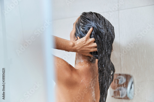 Brunette young woman washing her hair in shower