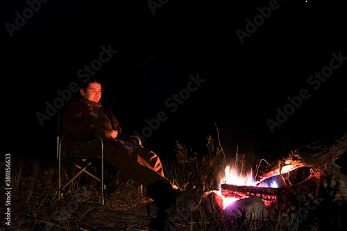 Tourist is taking a rest near campfire at night.