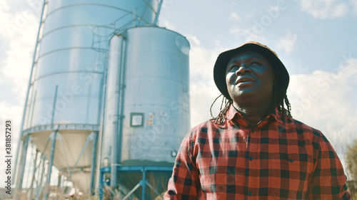 Young handsome african farmer standing in front of the silo system. High quality photo
