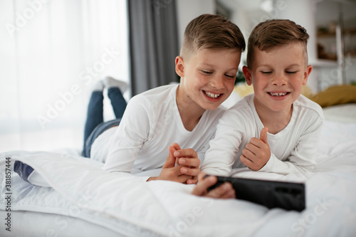 Two little brothers are playing games on the phone. Beautiful boys enjoying at home..