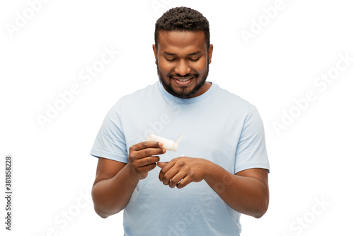 grooming, skin care and people concept - happy african american man applying moisturizer to his hand over white background