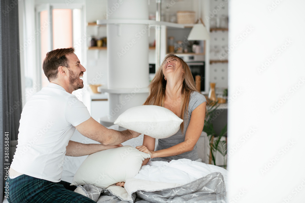Obraz premium Young couple fighting pillows on the bed. Happy couple having fun at home