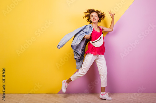 Full length shot happy woman in white jeans and pink shirt. Ecstatic girl with short curly hairstyle fooling around on yellow and pink background.
