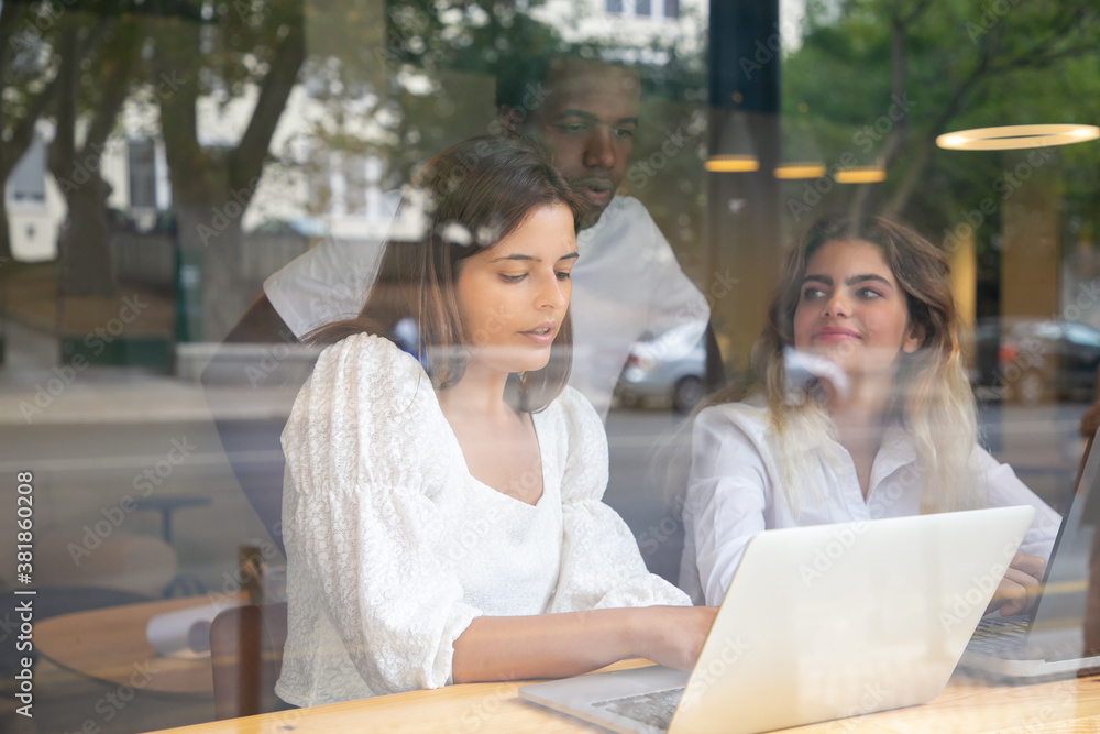 Brunette designer working with clients and showing design on laptop. Multiethnic colleagues talking about design and working indoors behind window. Communication and teamwork concept Brunette designer working with clients and showing design on laptop. Multiethnic colleagues talking about design and working indoors behind window. Communication and teamwork concept