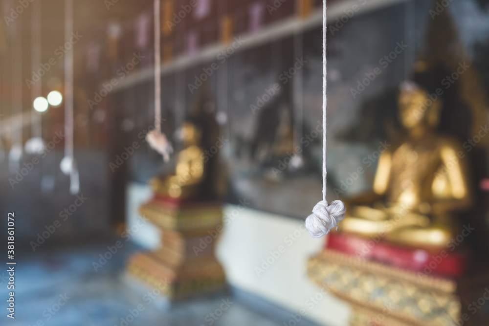 A white thread with a knot at a buddhist temple. Buddha statue in the background.