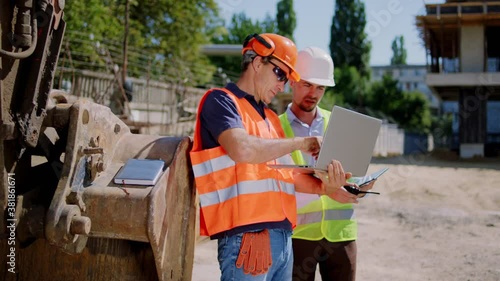 Middle-aged foreman and engineer guy with a protective uniform using the laptop to check the construction of building they have a discussing concentrated. 4k