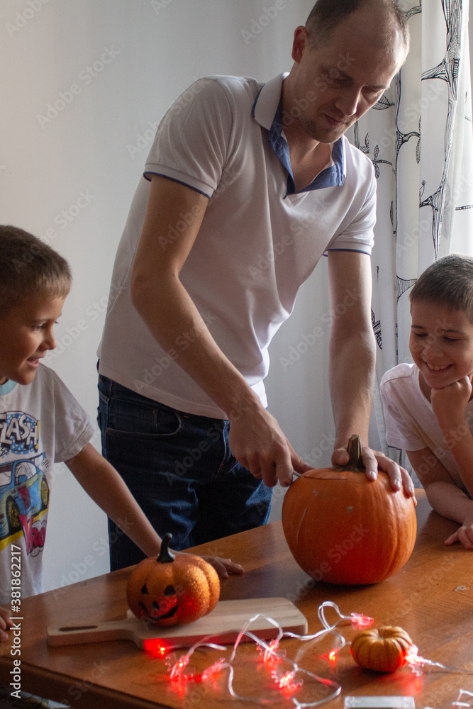 Fototapeta premium Dad and his sons make a pumpkin for halloween