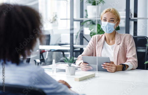 New normal and modern interview during covid-19 outbreak. HR manager with laptop looks at african american woman through protective glass