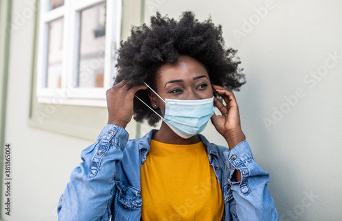 A young black woman stands alone on the street and puts a mask on her face, living during a virus pandemic photo