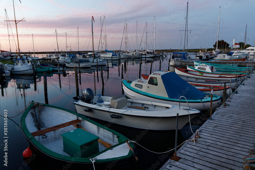 Hafenszene mit Segelbooten bei Sonnenuntergang, farbige Boote auf ruhigem Wasser vor rötlich bis bläulichem Himmel