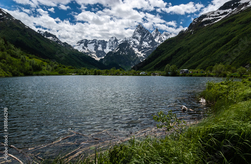 Mountain lake. Reed floats in the water, green and rocky snowy mountains surround the plain, blue sky. Caucasus., Russia