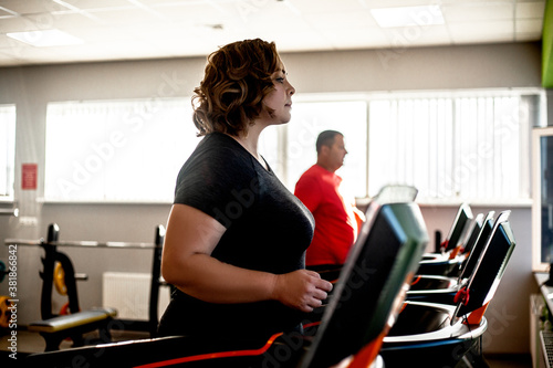 Fat woman fights overweight in the gym, doing heavy fitness exercises for future strong body. Obese person workout with sport equipment