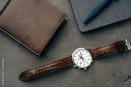 Male watch and leather wallet on dark grey surface