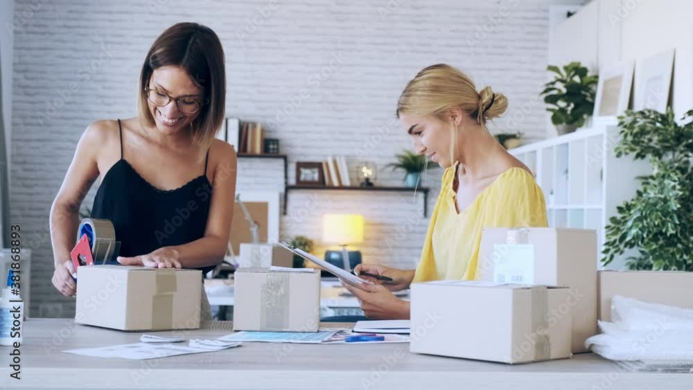 Video of two beautiful freelance business women seller checking product order while packing and sealing cardboard boxes for delivery products in their startup small business.
Video of two beautiful freelance business women seller checking product order while packing and sealing cardboard boxes for delivery products in their startup small business.