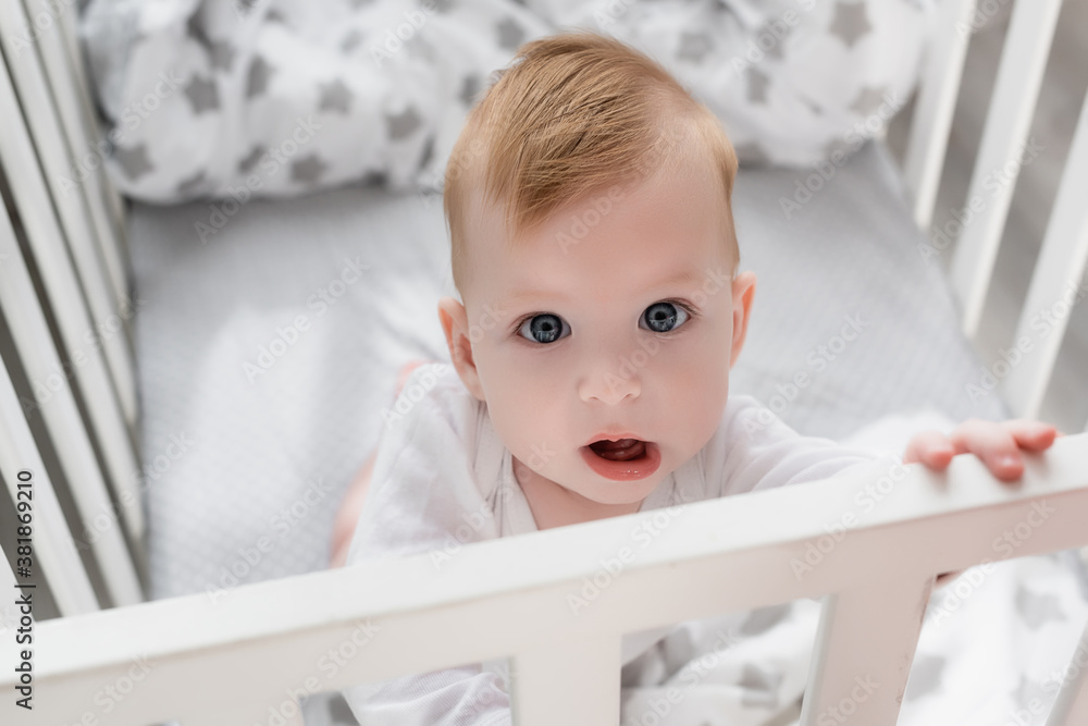 overhead view of baby boy looking at camera while standing in crib with open mouth overhead view of baby boy looking at camera while standing in crib with open mouth