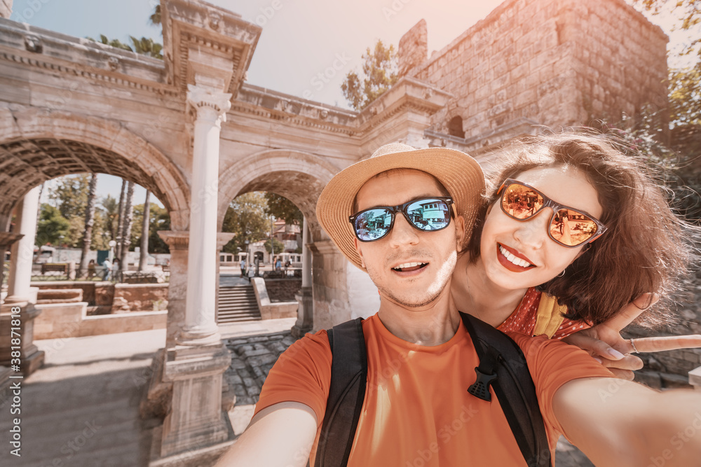 A man and a woman in love embrace and take a selfie photo against the backdrop of the archaeological ruins of Hadrian's gate in Antalya. Honeymoon in Turkey concept