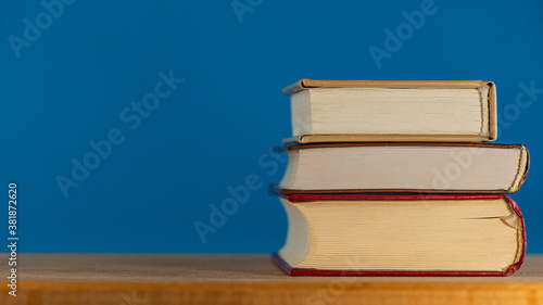 stack of three books lies on a blue background on an oak table.
