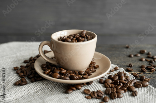 Coffee cup filled of fresh arabica or robusta coffee beans with scattered coffee beans on a linen textile and wood table.