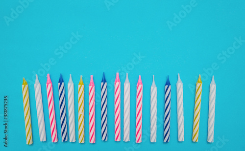 Colorful candles are placed in a row for a birthday cake on a blue background.