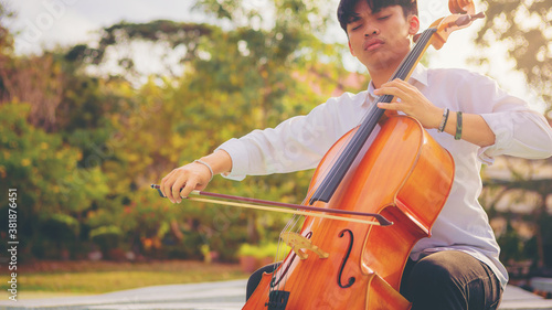 Musician man using a bow to practicing the cello playing with the melodiousness at the sunset. Selected focus.