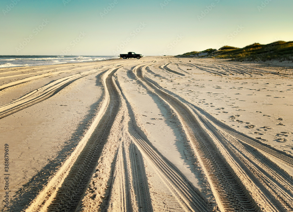 Fototapeta premium Sand tracks on the beach with black truck