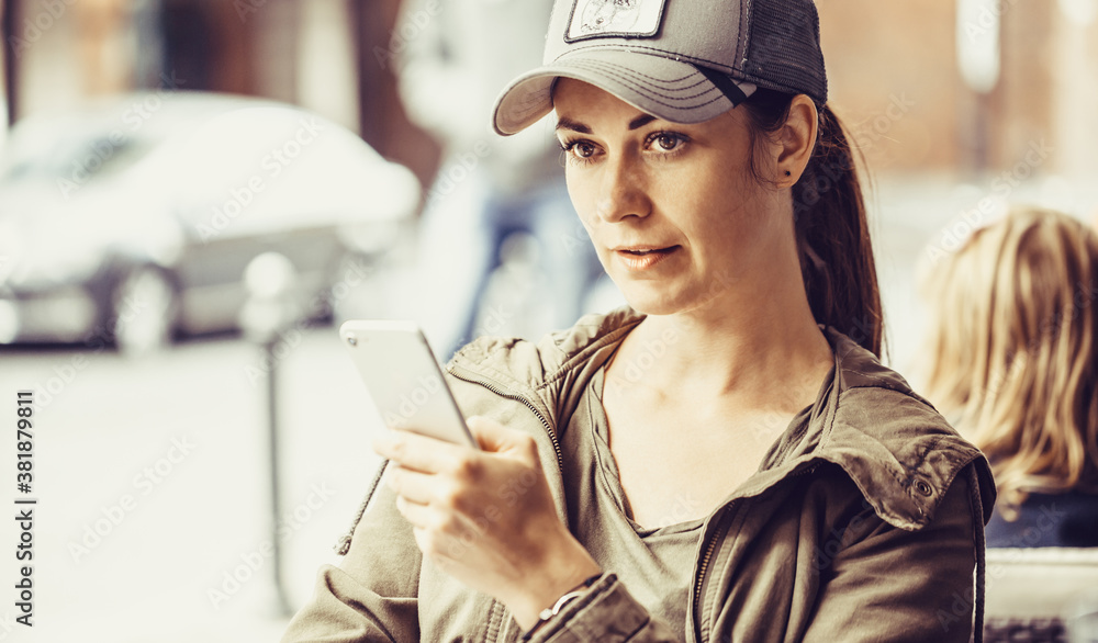 Millennial woman sits in a restaurant and uses a smartphone. Woman is waiting for food and browses social media on the phone. Shallow depth of field and focus aimed at the right eye. Millennial woman sits in a restaurant and uses a smartphone. Woman is waiting for food and browses social media on the phone. Shallow depth of field and focus aimed at the right eye.