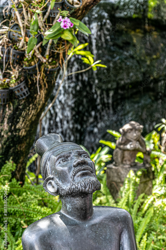 Fototapeta premium Estatua budista en jardín verde con agua y árbol al fondo