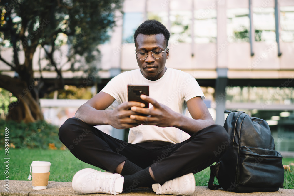 Black man messaging on cellphone and sitting on curb Black man messaging on cellphone and sitting on curb