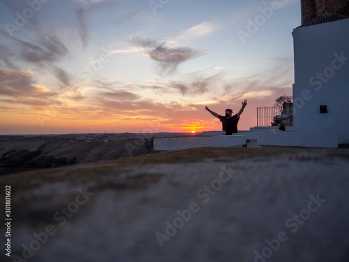 Фотография Hombre joven con los brazos abiertos en un mirador con la puesta de sol de fondo