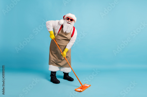Full body size photo of retired old man grey beard hold mop washing floor public janitor wear santa x-mas costume apron rubber glove suspender sunglass cap isolated blue color background