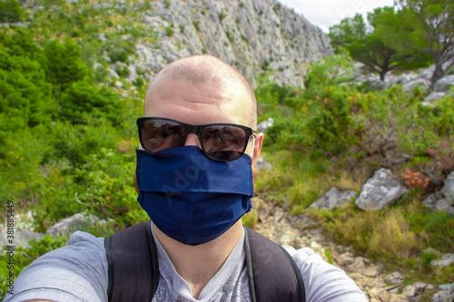Bald man wearing black sunglasses and a blue facemask taking a selfie while trekking, hiking in nature in Croatia. Exploring the nature in autumn during the covid global pandemic
