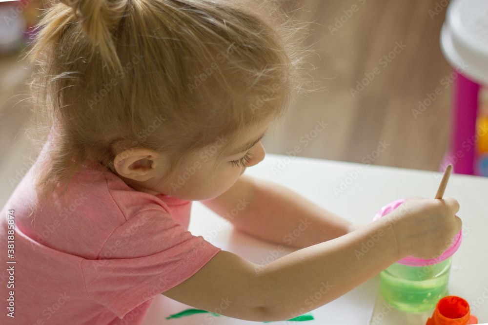 Fototapeta premium little girl painting with paintbrush and colorful paints.