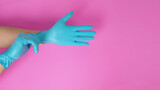 Hand is wear and pull  latex gloves on pink background.