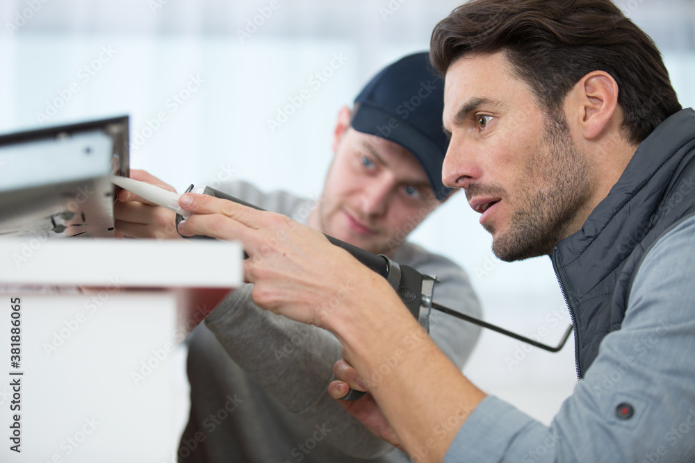 Obraz premium apprentice learning how to use caulking gun with teacher