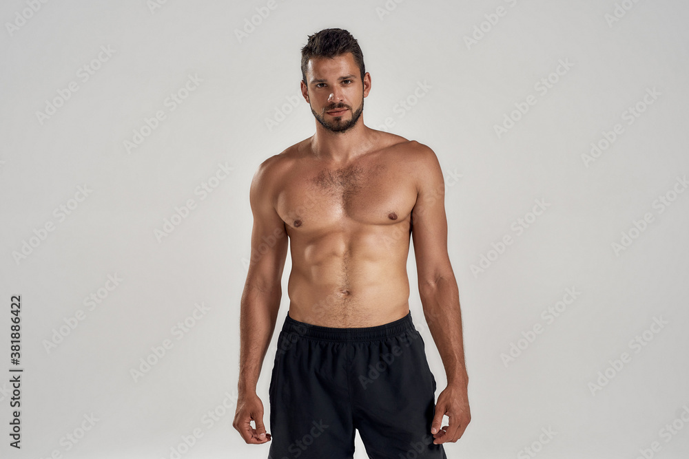 Young muscular caucasian man looking at camera while posing shirtless isolated over grey background Young muscular caucasian man looking at camera while posing shirtless isolated over grey background