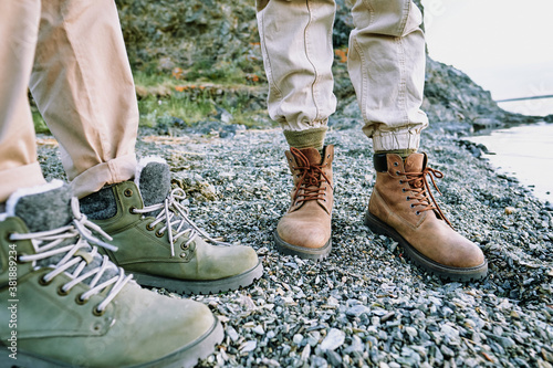 Close-up of unrecognizable couple standing in comfortable hiking boots on pebbles near water