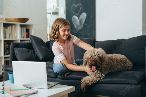 young girl sitting on sofa cuddling with her dog at home