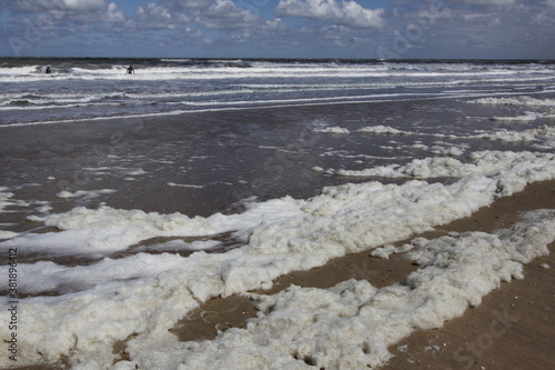Surfers walk into the stormy sea with lots of foam to go surfing.