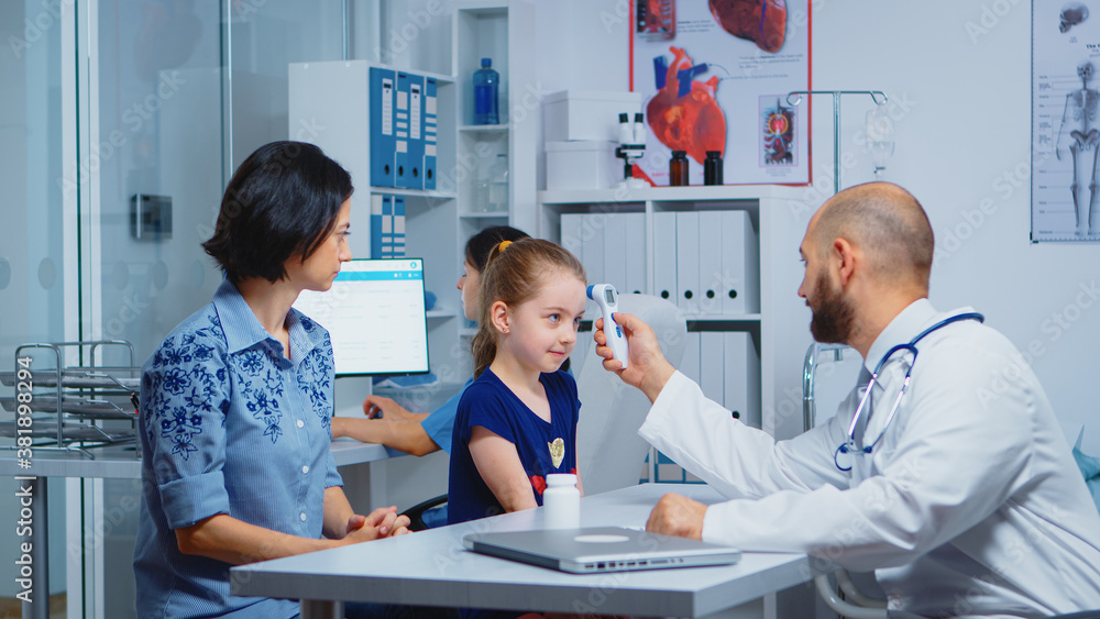 Pediatrician checking temperature and nurse writing on computer. Doctor specialist in medicine providing health care services consultation diagnostic examination treatment in hospital cabinet Pediatrician checking temperature and nurse writing on computer. Doctor specialist in medicine providing health care services consultation diagnostic examination treatment in hospital cabinet