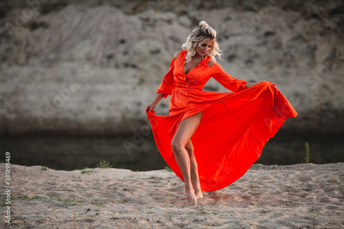 Beautiful woman in orange dress posing at the background of sand hill