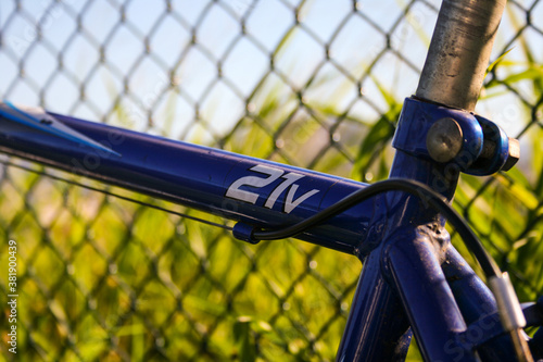 Detail of a blue 21v bike a little rusty. Chain-link fencing. Green field and blue sky in the background. Rio de Janeiro, Brazil. 2013