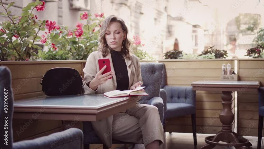Business woman in a suit talking on the phone in a cafe on the street. The entrepreneur plans his work by discussing it with clients. Business woman in a suit talking on the phone in a cafe on the street. The entrepreneur plans his work by discussing it with clients.
