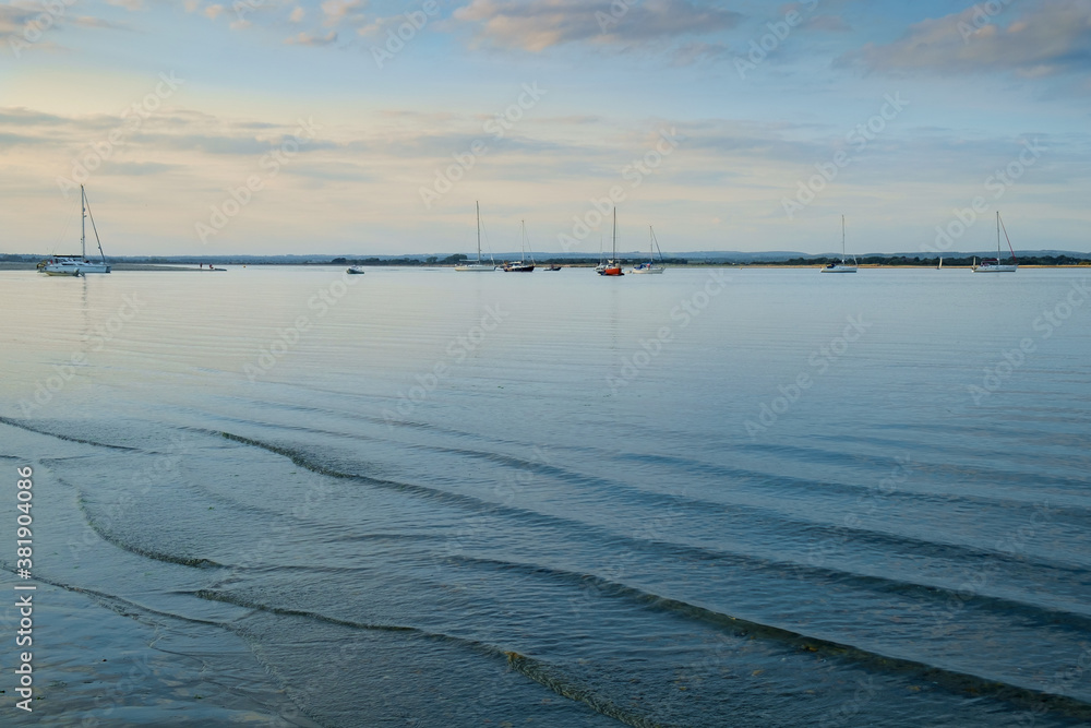 West Wittering, Chichester Harbour, South of England. Small waves gently lap onto the shore in the evening light. West Wittering, Chichester Harbour, South of England. Small waves gently lap onto the shore in the evening light.