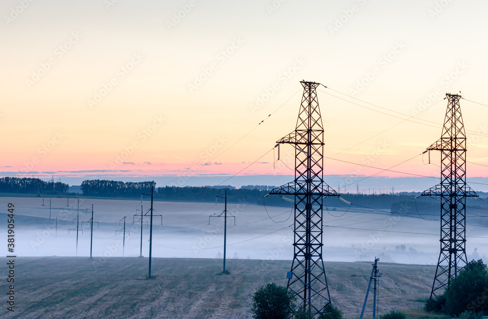 Landscape with supports for high-voltage wires and fog at dawn