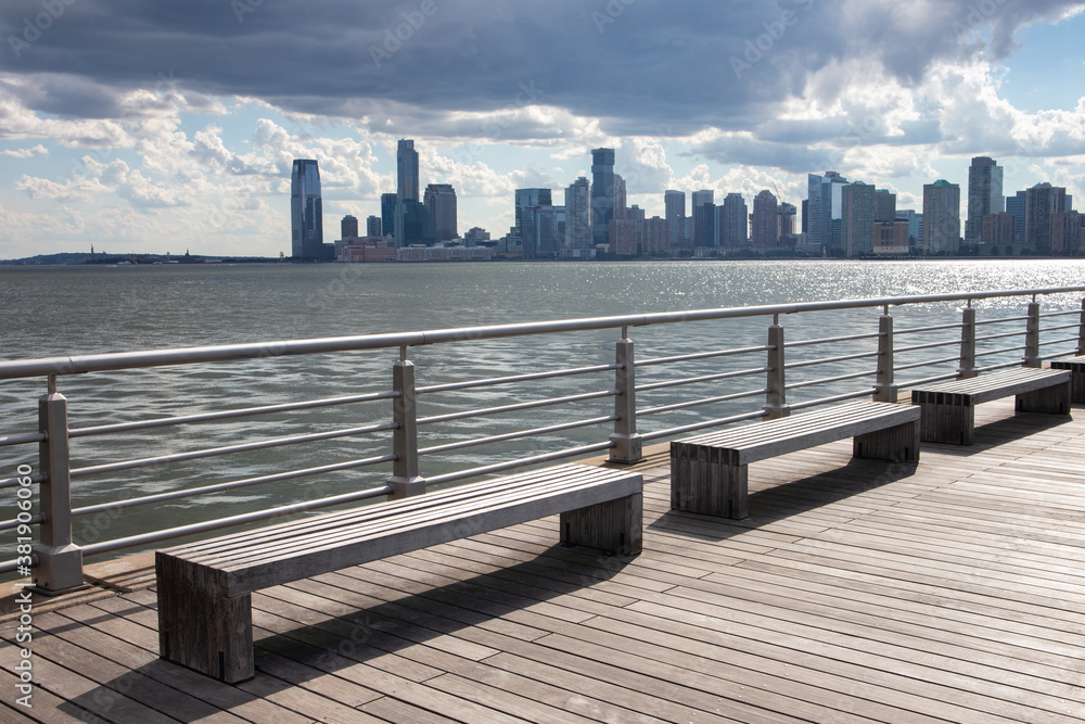 Row of Empty Benches on a Pier along the Hudson River in New York City with a view of the Jersey City Skyline