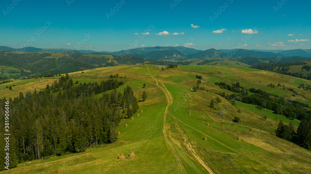 Beautiful aerial view to green hill and great mountains under blue sky. Long mountain range and long valley with forest. Awesome alpine landscape in sunny day.