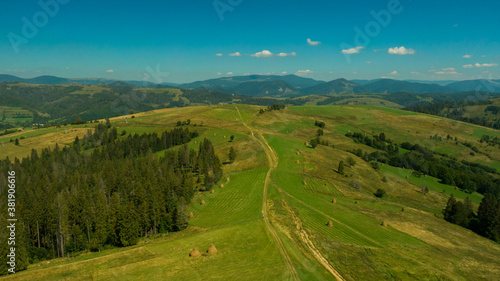 Beautiful aerial view to green hill and great mountains under blue sky. Long mountain range and long valley with forest. Awesome alpine landscape in sunny day.