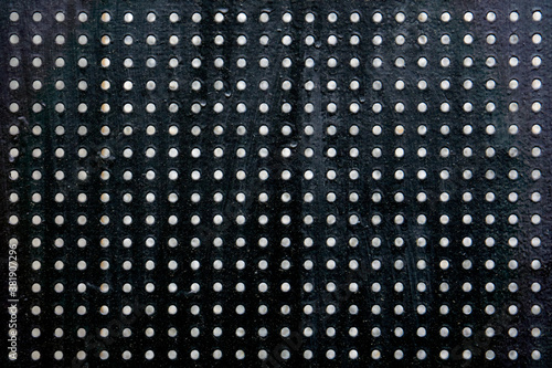 Black perforated steel sheet with round holes, close-up.
