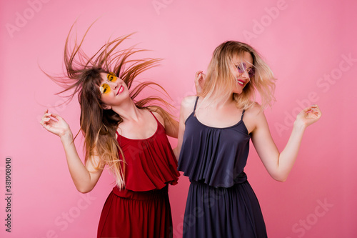 Two carefree female having fun and dancing on pink background. Flash portrait. Party mood . Similar dress. Friendship concept.