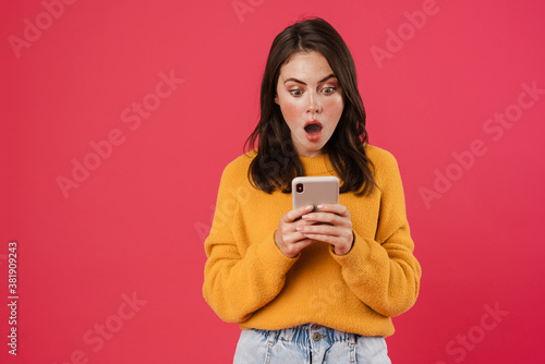 Image of shocked brunette girl posing and using mobile phone